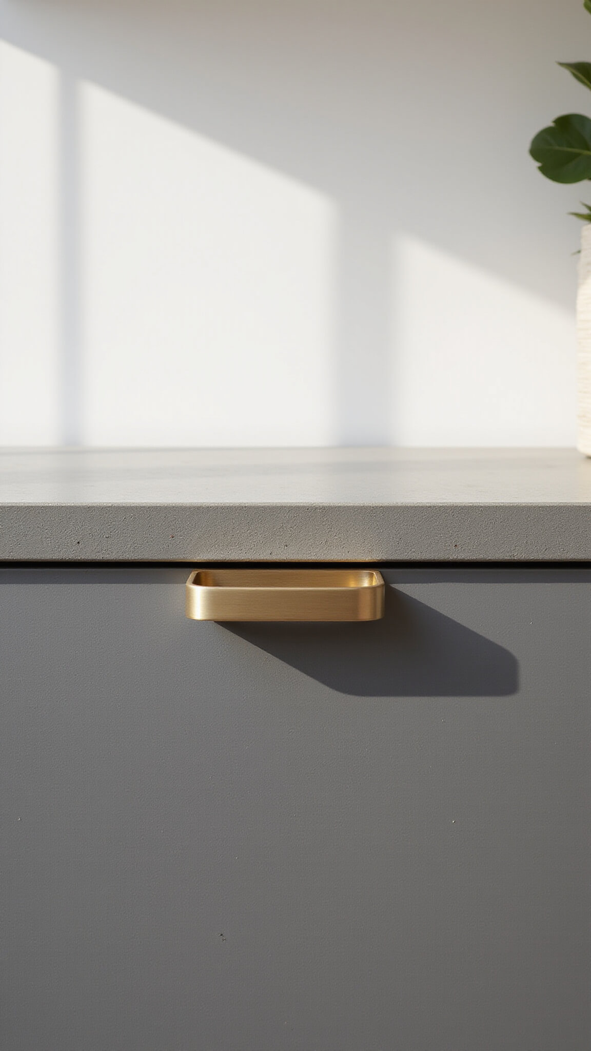 Close-up of textured concrete cabinet with brushed brass handle in soft afternoon light, showing detailed surface variations and craftsmanship.