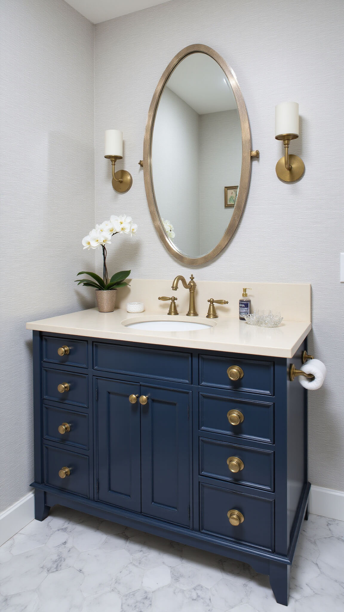 Transitional powder room with hexagonal marble floor tiles, navy vanity with brass hardware, quartz countertop, brass faucet, round mirror, and light gray textured wallpaper.