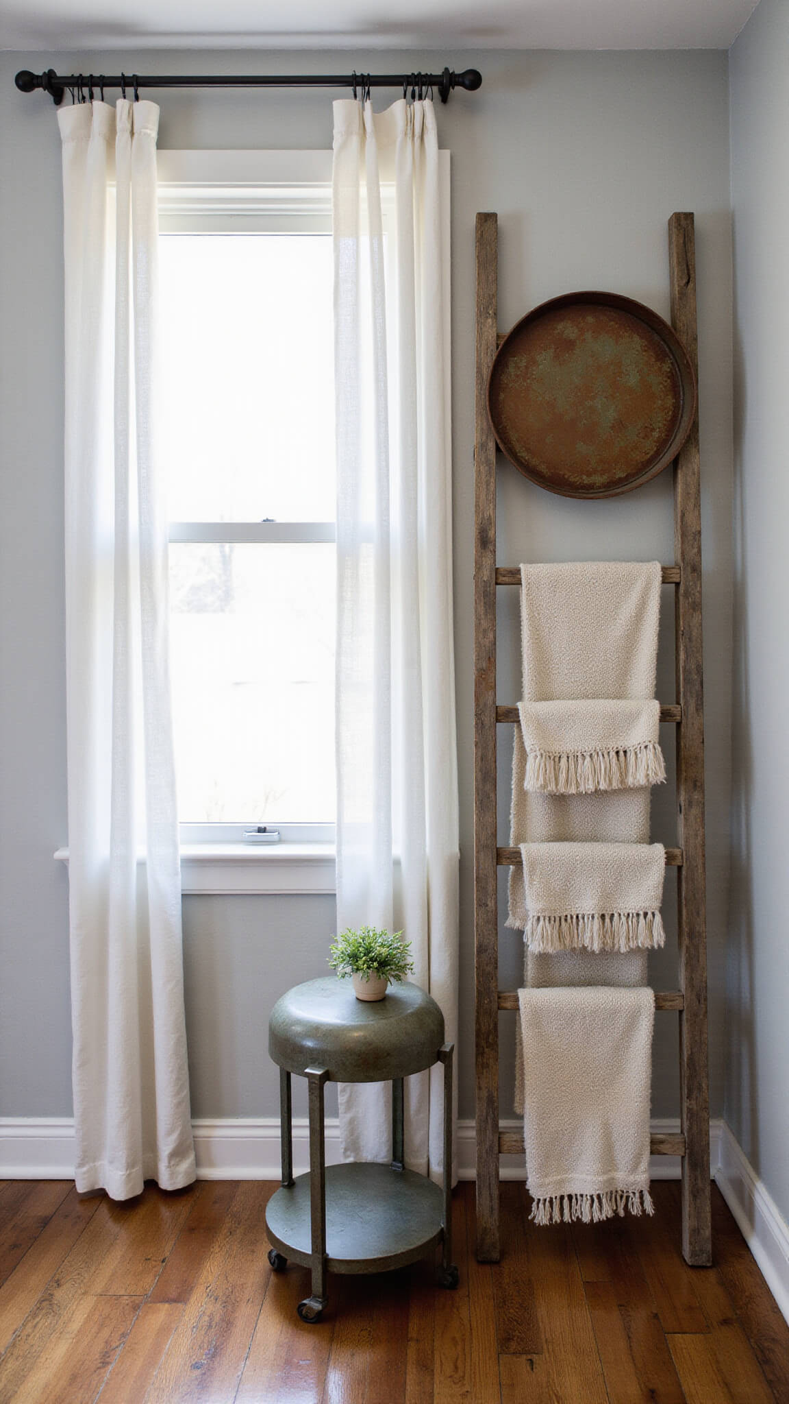 Industrial farmhouse corner with vintage cart side table, rusted metal mirror, wooden ladder with textiles, and soft morning light highlighting layered textures.