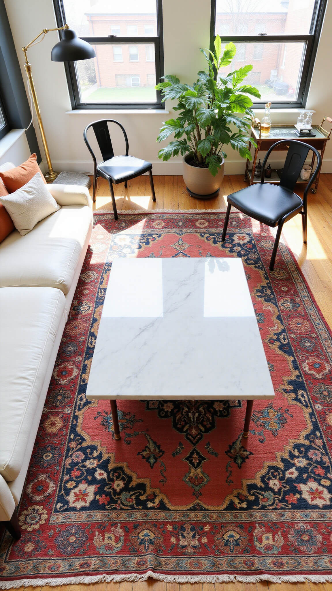 Bird's-eye view of a sunlit 22x25ft open-concept room featuring a white sectional, 1970s Italian marble coffee table, black bentwood dining chairs, vintage jewel-toned Turkish kilim, large philodendron in a planter, and brass and smoked glass bar cart with mixed barware.