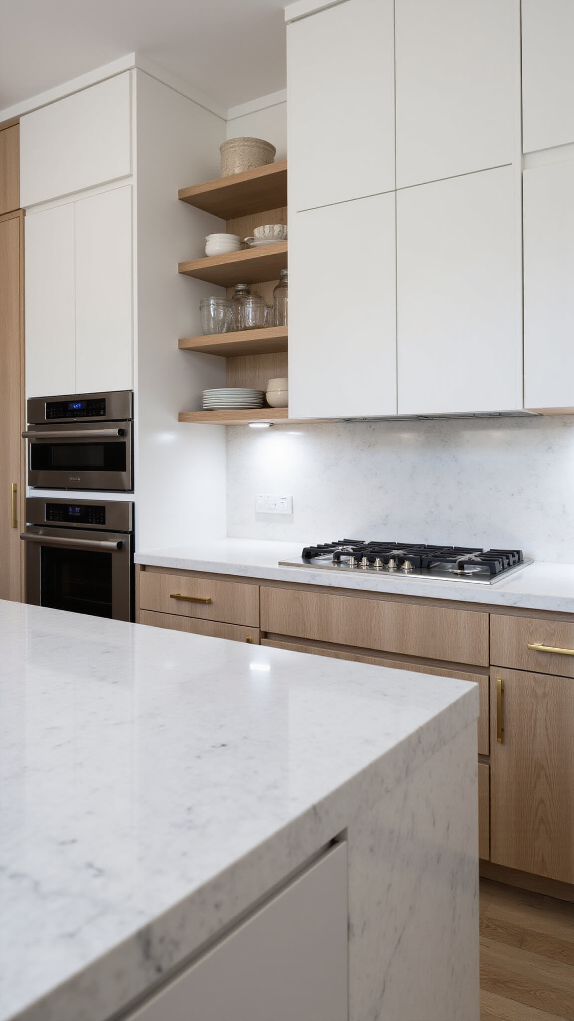 Modern minimalist kitchen with marble waterfall island, white oak cabinets, matte white uppers, brass accents, and curated open shelving at dawn.