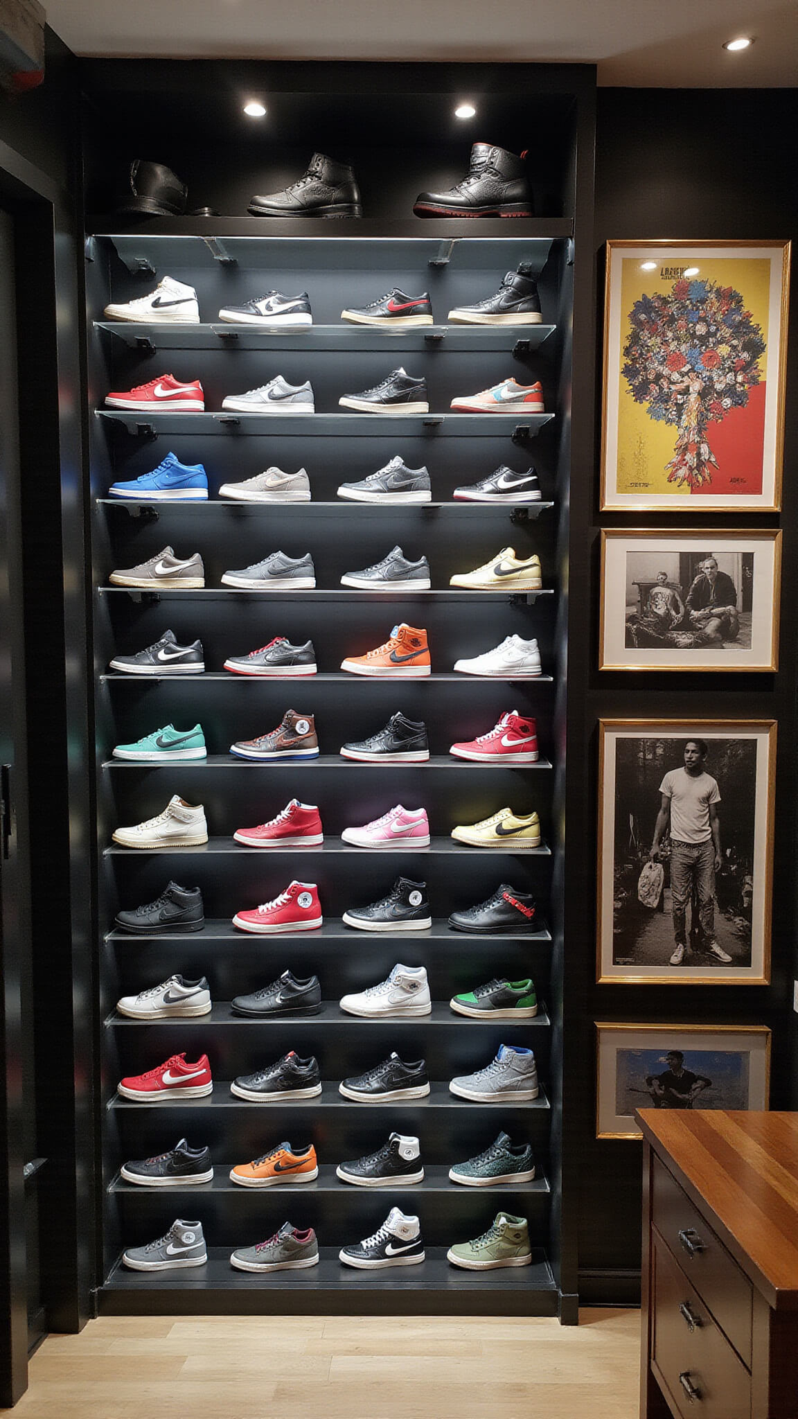 Streetwear walk-in closet with matte black grid storage, floating acrylic shelves displaying limited-edition sneakers, vintage concert posters, and Supreme accessories under dramatic LED spotlighting.