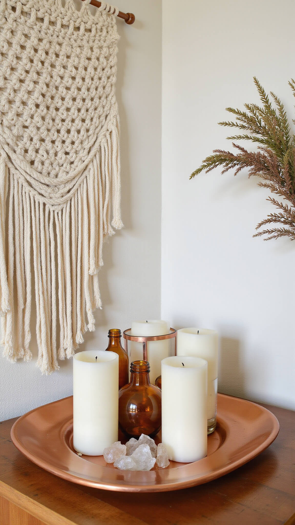 Close-up of altar corner with macramé wall hanging, candles, crystal grid on copper tray, and dried herbs in warm afternoon light.