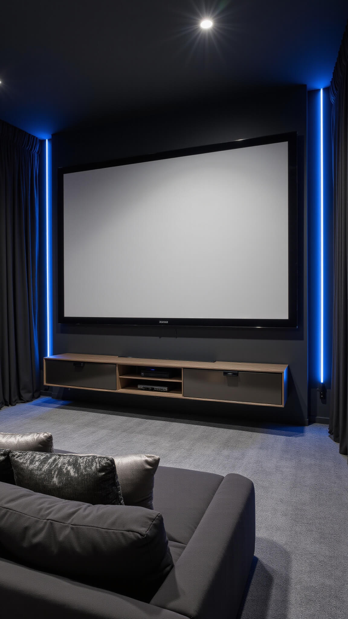 Modern minimalist home theater with black walls, white projector screen, charcoal velvet sectional, metallic accents, and electric blue LED lighting.