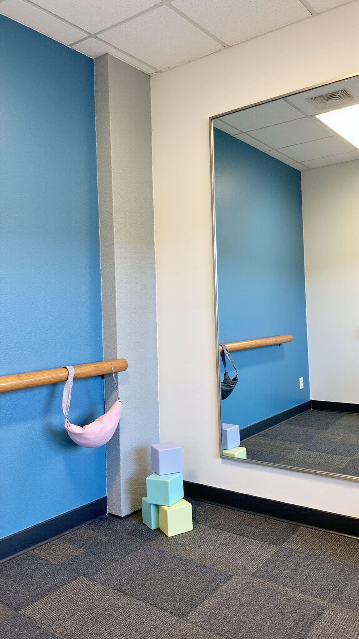 Sensory corner with blue textured wall, floor-to-ceiling mirrors, pastel foam blocks, bubble chairs, and geometric carpet tiles, viewed from child’s perspective in soft morning light.