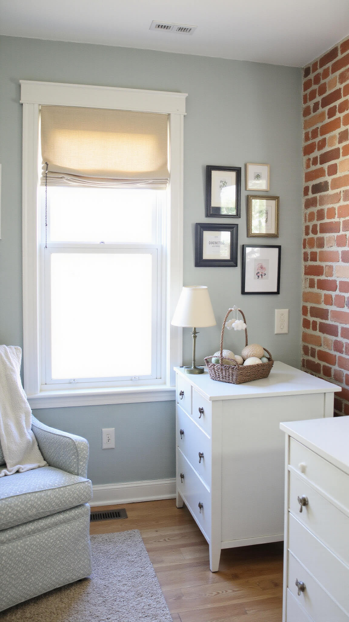 DIY budget nursery with painted brick accent wall, upcycled vintage crib, gallery wall of thrifted frames, handmade felt cloud mobile, and painted dresser in soft natural light.