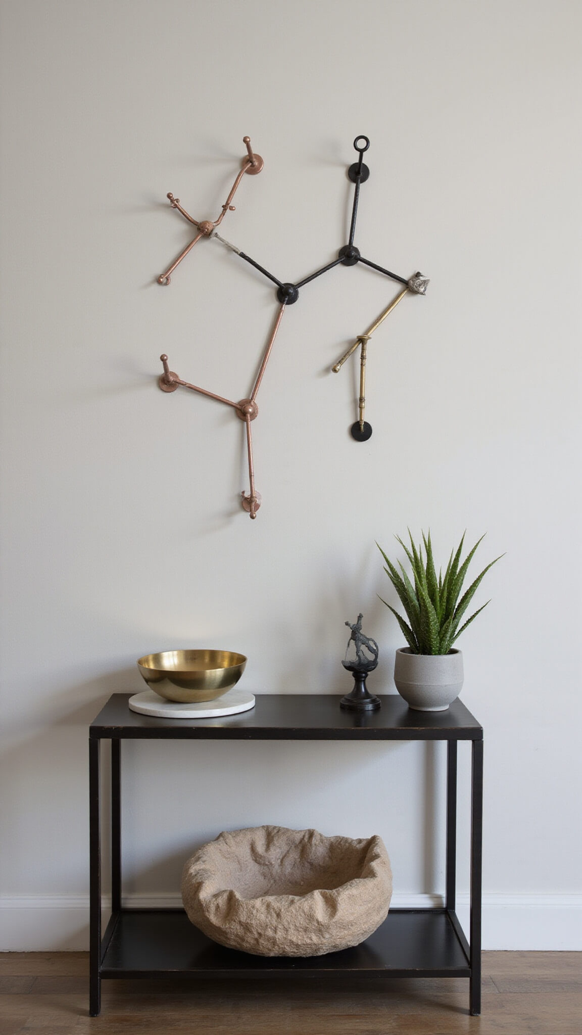 Macro shot of modern entryway with mixed metallic hooks on white wall, blackened steel console below holding marble tray, brass key bowl, and sculptural air plant, softly lit at dusk.