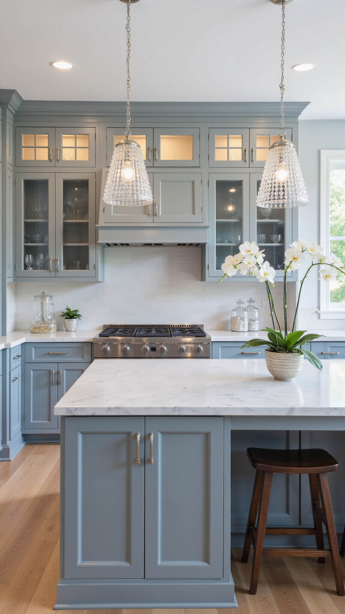 Transitional 15x17ft kitchen with gray-teal cabinets, Carrara marble surfaces, crystal pendant lights, white oak flooring, and elegant decor.