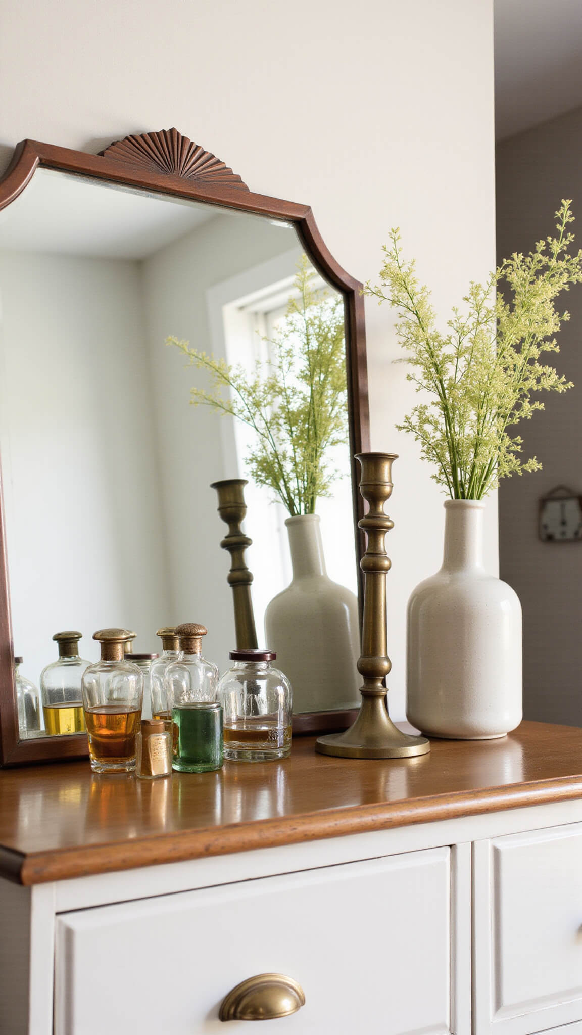 Curated dresser top with vintage perfume bottles, brass candlesticks, and a ceramic vessel, lit by mid-morning light reflected in an art deco mirror.