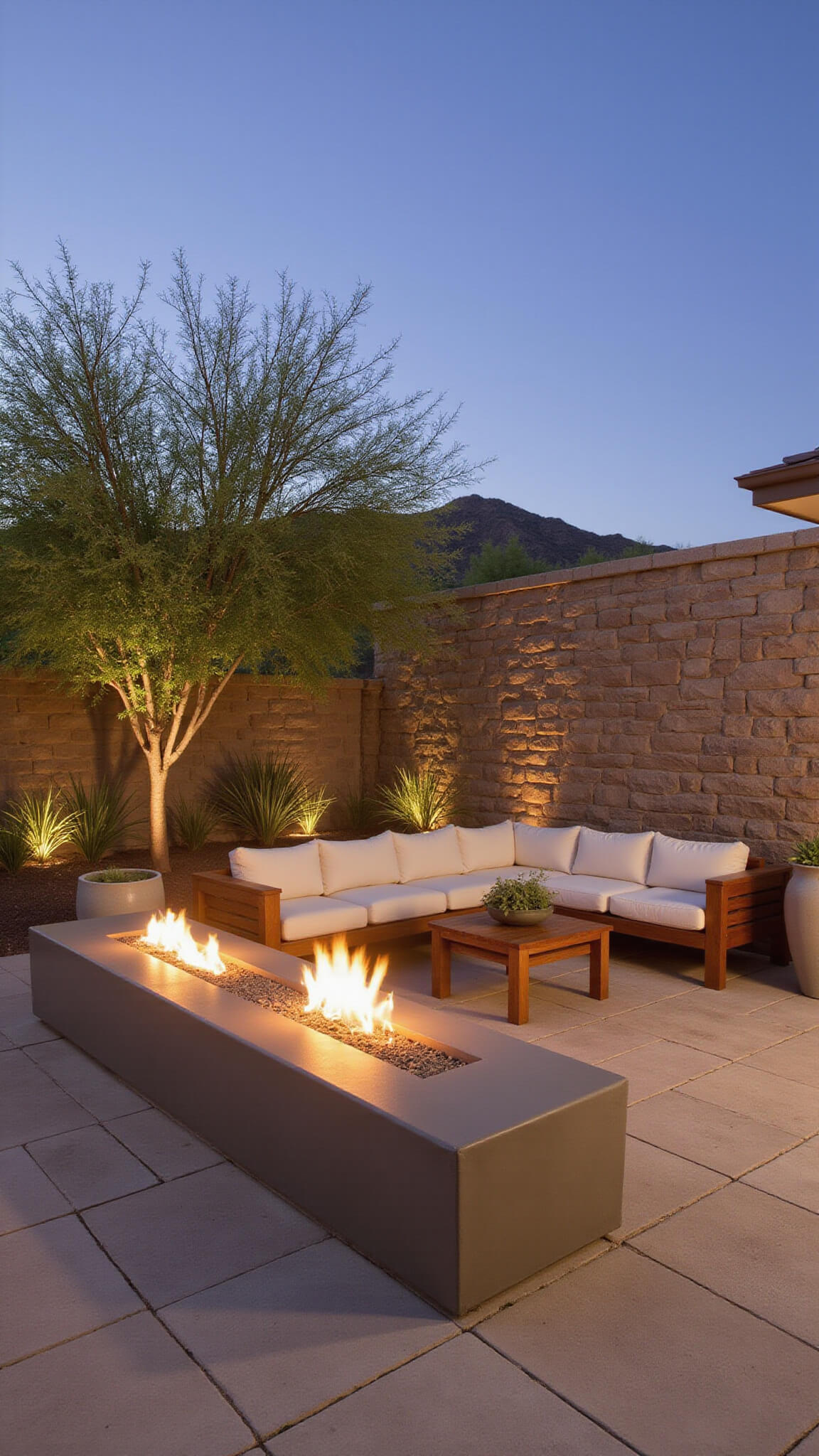 Desert modern fire lounge at dusk with travertine patio, floating concrete bench with linear gas fire, low-profile teak sectional, and large succulents in ceramic planters.