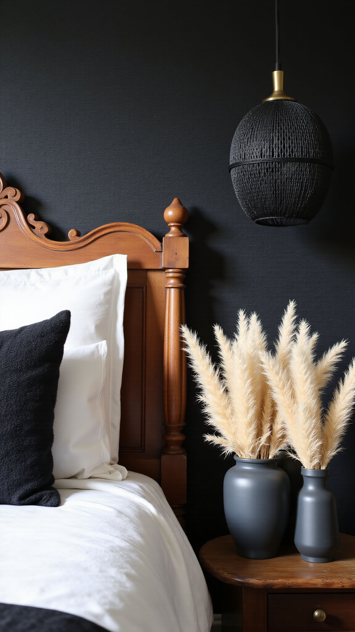 Close-up of black grasscloth wallpaper behind vintage wooden headboard in textured bedroom with layered white, black, and copper bedding, black woven pendant casting shadows, and pampas grass in matte black vases.