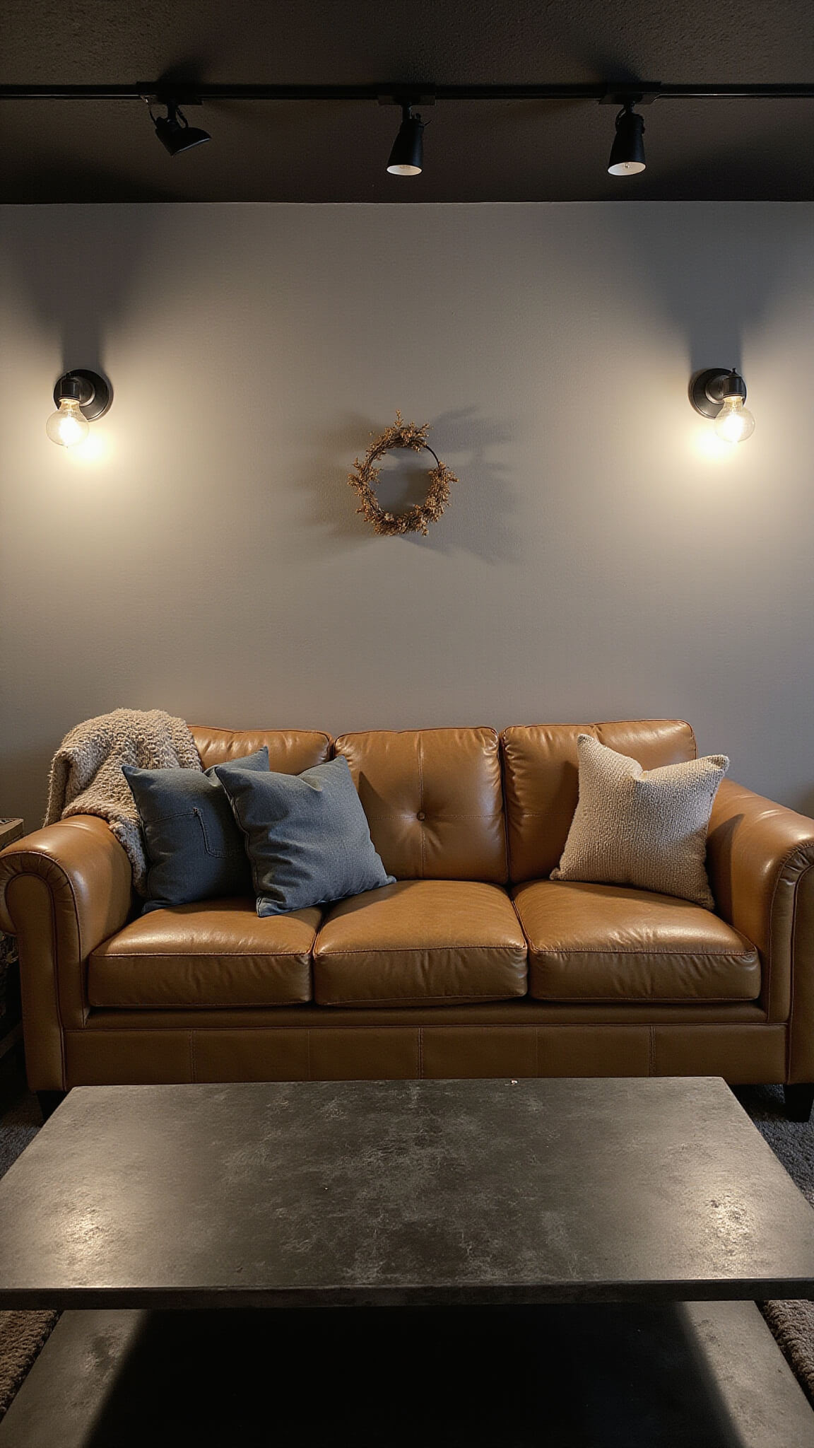 Moody industrial-style living room with camel leather tufted sofa, raw steel coffee table, vintage factory cart side table, and warm filament sconce lighting.