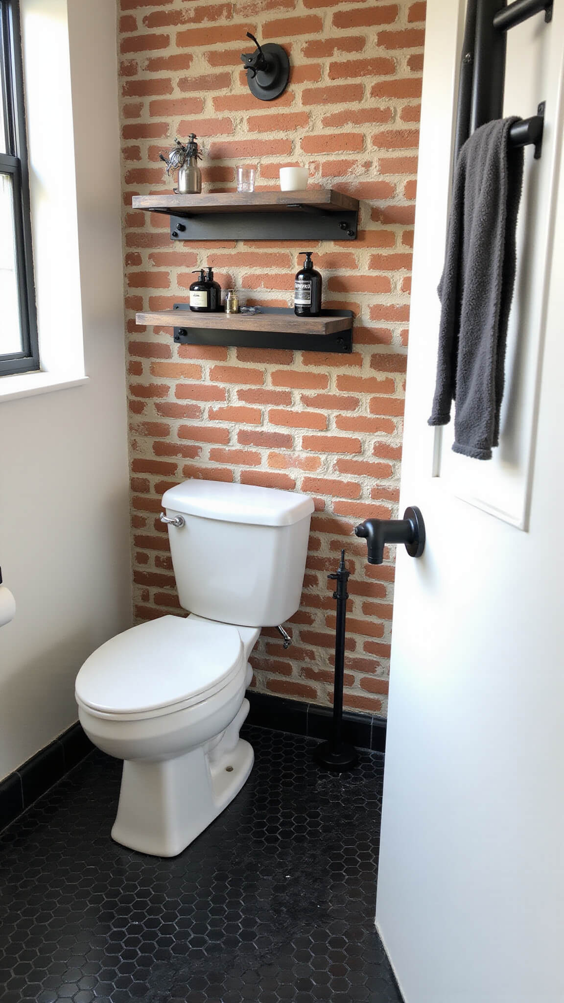 Modern urban industrial bathroom with exposed brick wall, black hex tile floor, matte black fixtures, floating metal shelves, and dramatic natural lighting.