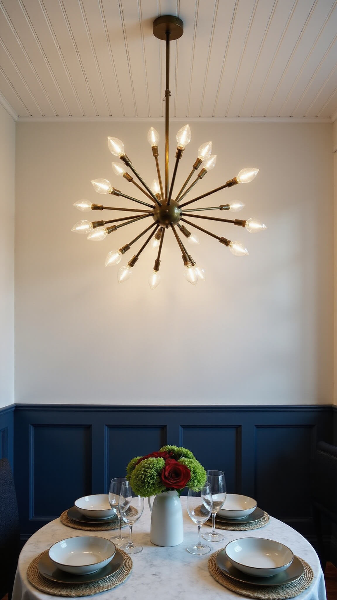 Elevated view of a navy-walled kitchen dining nook with a brass sputnik chandelier casting shadows over a round marble table set with ceramic plates and crystal wine glasses.