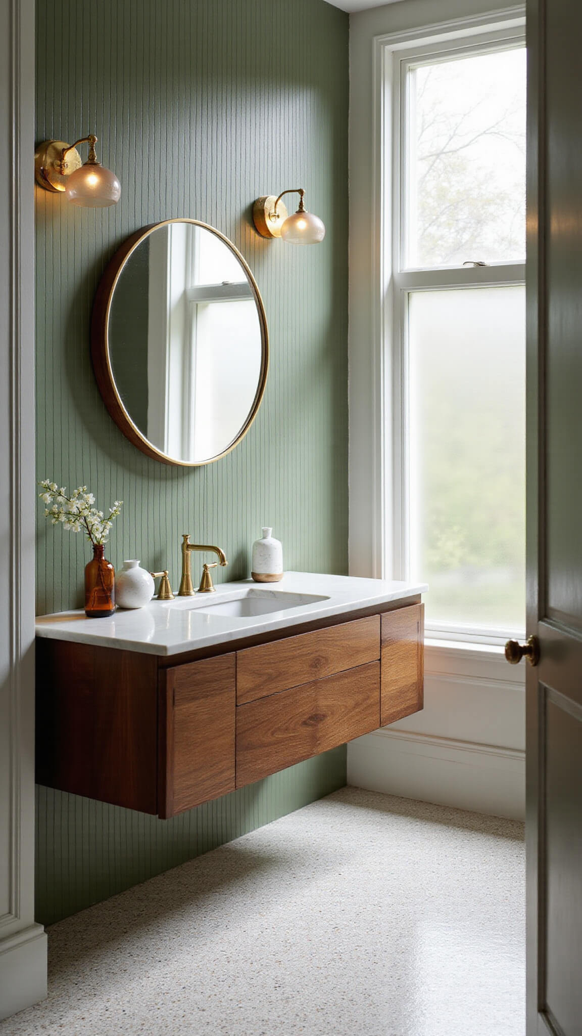 Modern 10x12ft bathroom with sage green tile accent wall, floating walnut vanity, brass accents, terrazzo floor, and morning light through frosted window.