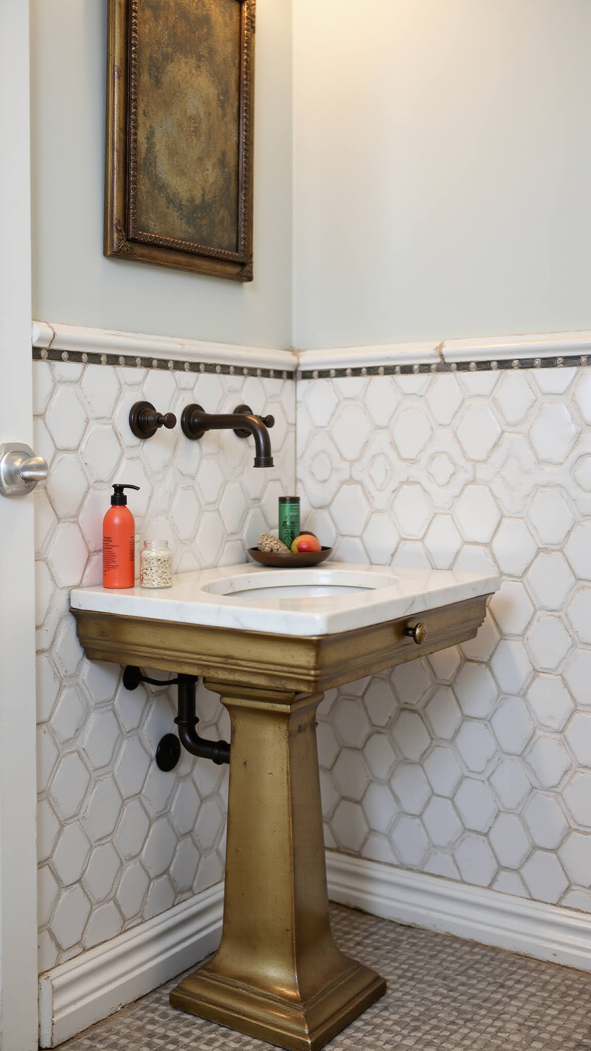 Close-up of vintage-modern powder room showing antique brass vanity with marble top, hand-painted tiles transitioning to penny rounds, and oil-rubbed bronze fixtures under directional lighting.