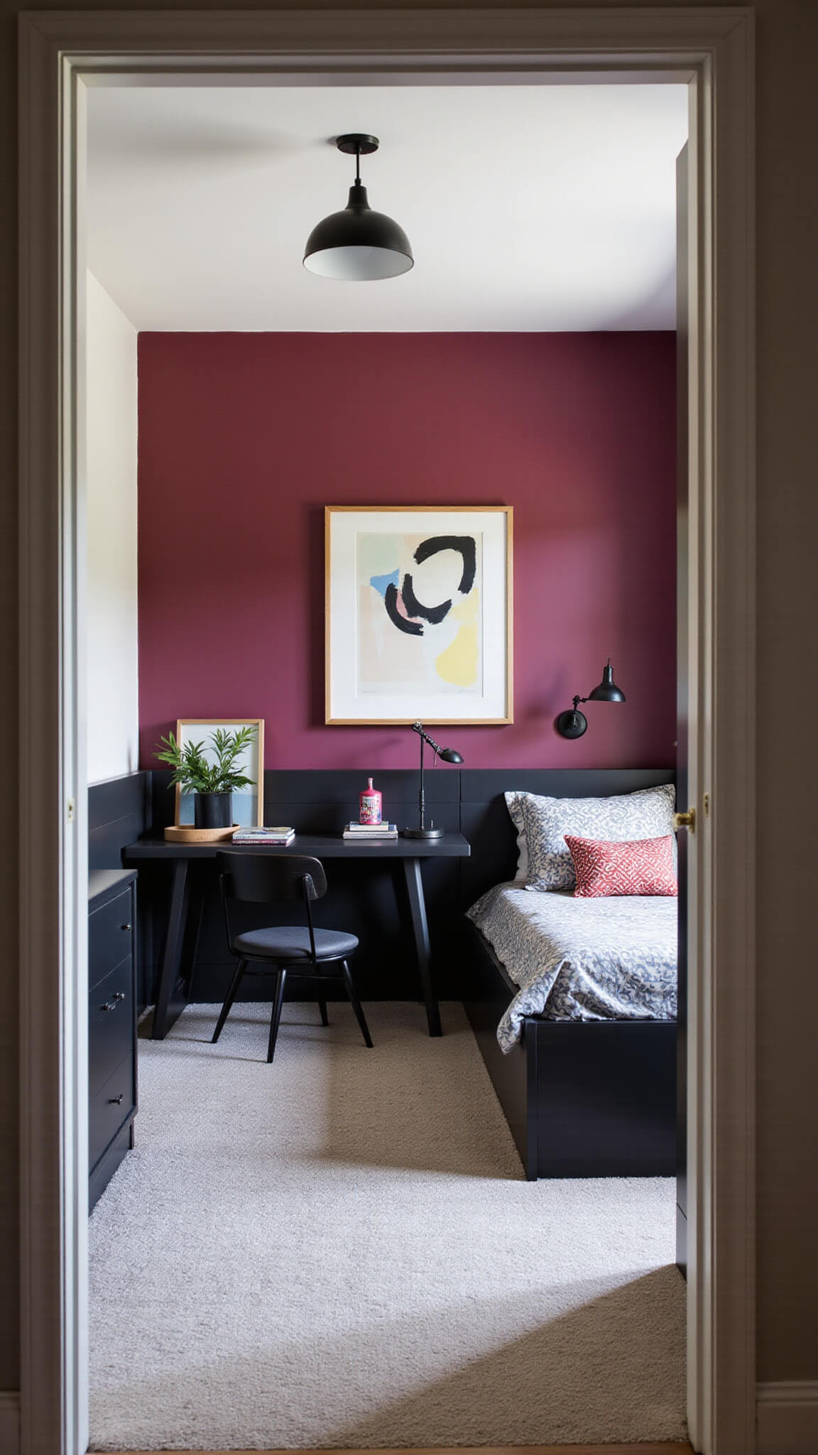 Teen bedroom with dark raspberry accent wall, mid-century black furniture, geometric bedding, built-in desk, and industrial lighting, viewed wide-angle from doorway.