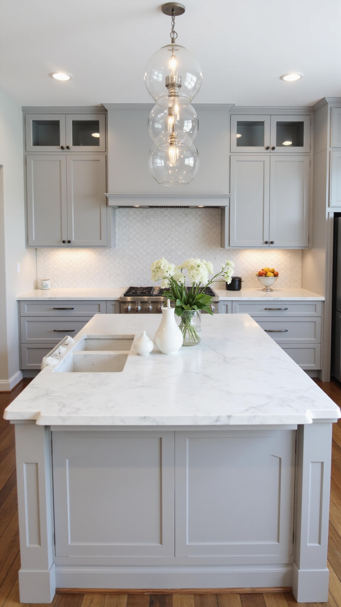 Bright contemporary gray and white kitchen with pearl gray cabinets, Carrara marble surfaces, glass uppers, chrome accents, and geometric layout viewed from above.