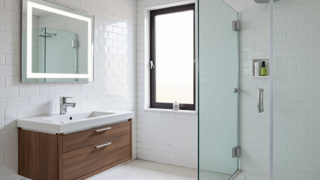 "Modern minimalist bathroom with white subway tiles, walnut vanity, LED mirror, and glass shower in morning light"