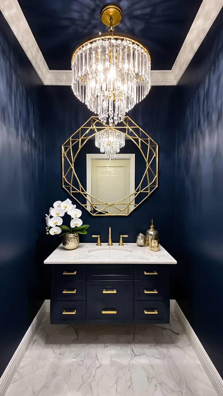 Glamorous navy powder room at night with sparkling crystal chandelier, gold mirror, marble vanity, and elegant decor.