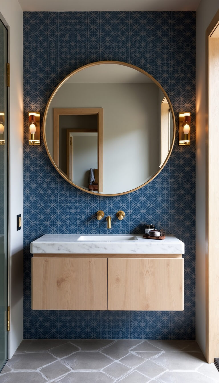 Modern Mediterranean bathroom with bleached oak floating vanity, deep blue zellige tile wall, round mirror with leather strap, grey geometric floor tiles, and brass fixtures.